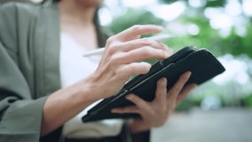 Close up shot Asian woman using smartpen write down on tablet with green leaf and trees background, urban lifestyle for new generation, smart technology wireless connection gadget creative application - Powered by Shutterstock - Get 15% off with code: PIKWIZARD15