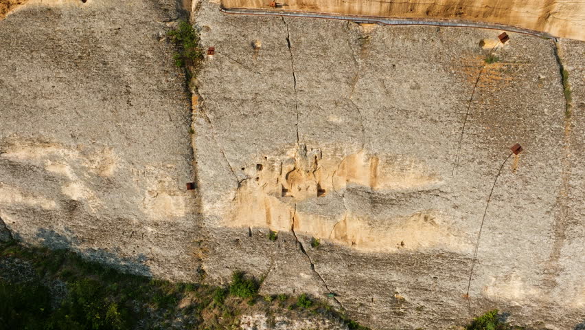 Monumental Madara Horseman relief carved in limestone rock face, drone view over Bulgaria’s summer fields and green woodland, UNESCO archaeological site, historic Balkan destination, cultural symbol