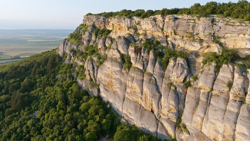 Flying over Madara Rider, ancient rock relief in Bulgaria Shumen Province, drone view of cultural monument and nature, green forests and fields, limestone plateau, summer sunlight enhances historical