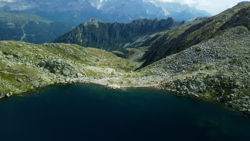 Drone footage starting at a mountain lake, ascending to reveal a green valley and storm clouds over rocky peaks. Ideal for dramatic nature, weather, and landscape content.