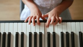 Close-up view of a young girl’s hands playing piano keys at home. Child in a white dress practicing music indoors. Concept of early music education, childhood creativity, and home learning. - Powered by Shutterstock - Get 15% off with code: PIKWIZARD15