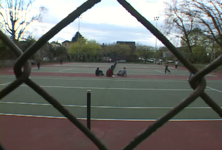 People play tennis at park in Portland, hand grabs fence.
