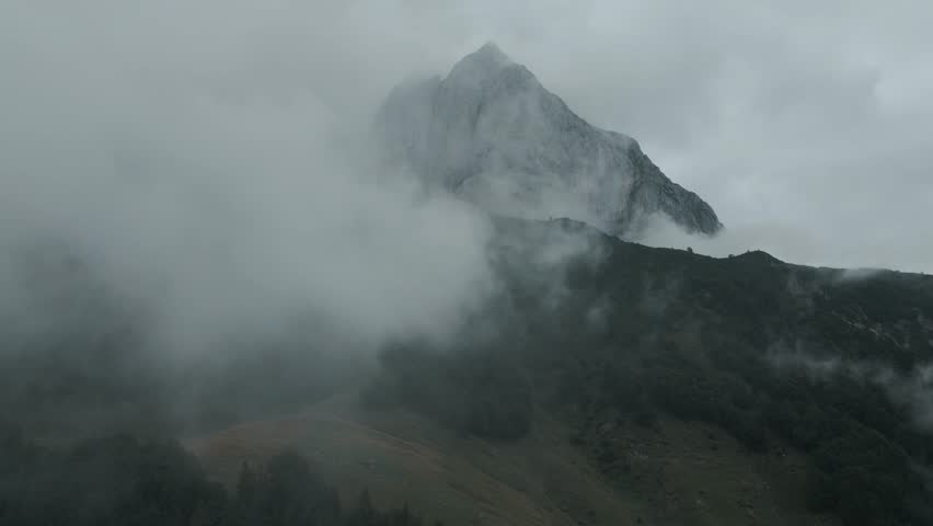 Aerial view of a majestic mountain peak piercing through ethereal mist, its rugged slopes contrasting with the soft, enveloping fog, Sankt Johann, Tyrol, Austria.