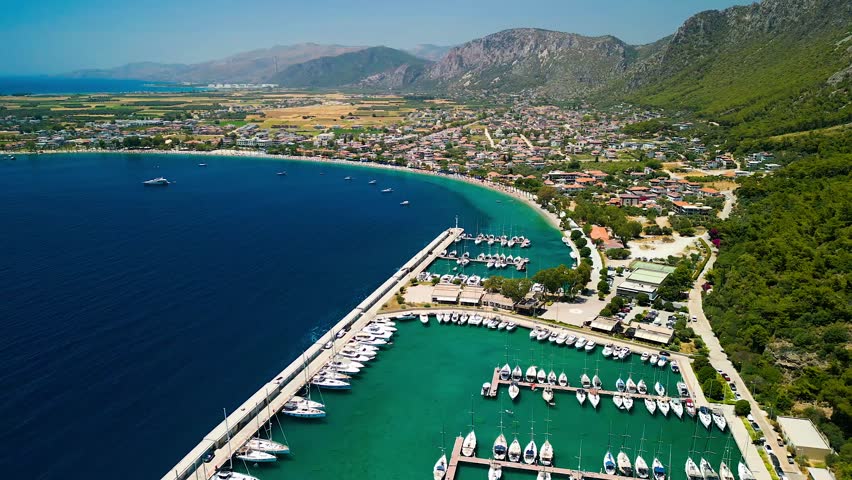 Aerial view of boats docked at Oren Marina, the turquoise sea contrasts with the golden beach and green hills, Oren, Mugla, Turkey.