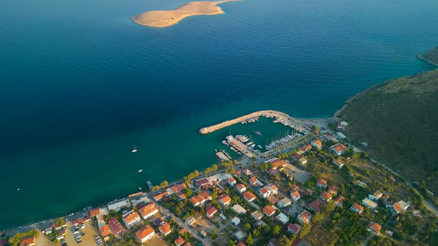 Aerial view of the harbor and boats contrasting with the deep blue sea and the island, with houses along the shore, Palamutbuku, Datca, Turkey.