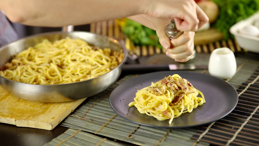 Grinding Pepper Onto Freshly Made Carbonara Pasta. Chef Seasoning Traditional Italian Dish. Delicious Homemade Meal. Gourmet Cooking. Flavorful Dinner Pasta Recipe. Creamy Sauce Pasta. Italian Cuisine