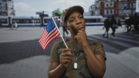 African american woman in camouflage military uniform points finger and holds us flag on street; patriotism defiance. - Powered by Shutterstock - Get 15% off with code: PIKWIZARD15