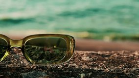 Stylish green retro sunglasses on a textured surface, perfect for a sunny day at the beach. Close-up shot of vintage sunglasses resting on a rocky surface with a blurred background of sky and wavy sea - Powered by Shutterstock - Get 15% off with code: PIKWIZARD15