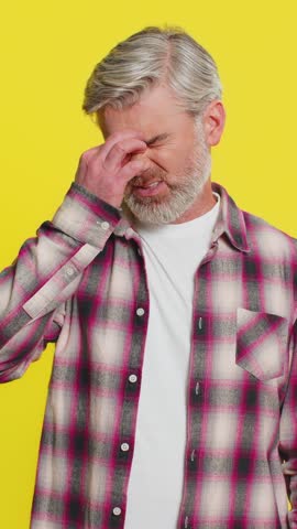 Mature man slowly removes glasses, revealing eye strain, exhaustion pain discomfort after long working hours. Middle-aged guy on yellow background displays fatigued face from continuous job tasks.