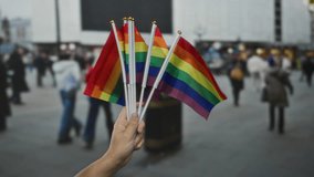 Hand holding rainbow flags in a busy city street with diverse people walking, symbolizing lgbtq pride, diversity, and inclusion in an urban outdoor setting. - Powered by Shutterstock - Get 15% off with code: PIKWIZARD15
