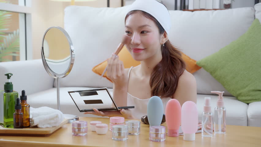 Beauty happy young asian woman applying makeup with brush looking mirror in living room at home, beautiful woman applying make-up with cosmetic on facial for glamour and elegant, make up and cosmetic.