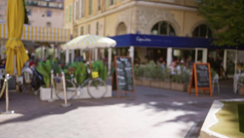 Blurry scene of a street cafe in marseille with people dining under umbrellas surrounded by defocused bicycles and decor.