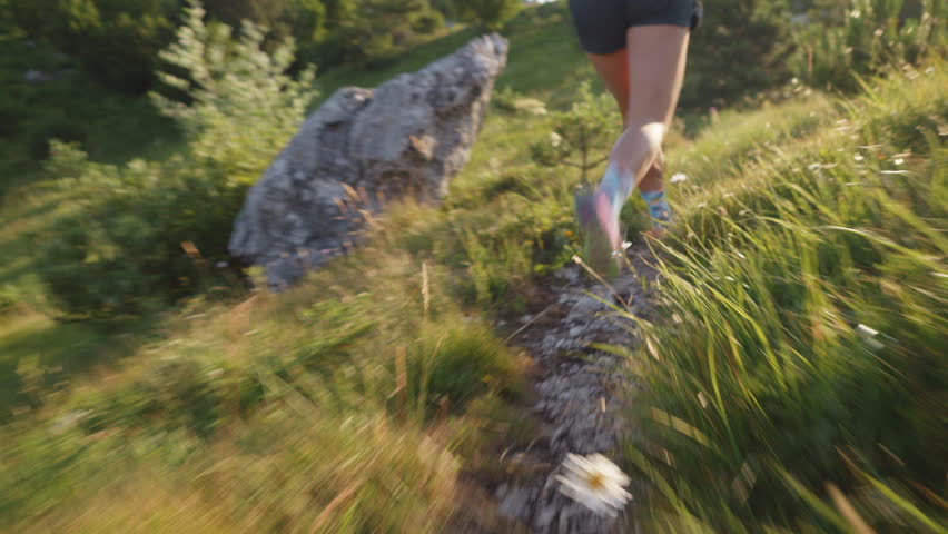 A trail runner in athletic gear sprints on a scenic dirt path, surrounded by greenery and wildflowers. The panning shot captures the dynamic motion of cross-country running, highlighting endurance.
