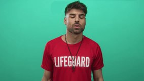 Young hispanic lifeguard man in red shirt holds binoculars to eyes against a green studio wall; vigilance. - Powered by Shutterstock - Get 15% off with code: PIKWIZARD15