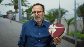 Man holding heart-shaped gift in outdoor urban park with blurred background and palm trees suggesting warmth and affection. - Powered by Shutterstock - Get 15% off with code: PIKWIZARD15
