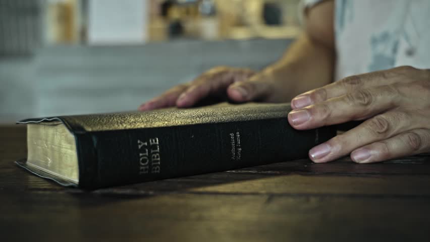 man open the book of the bible and read it on a wooden table daytime	