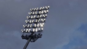Video capturing a large stadium floodlight illuminated against a dramatic, cloudy sky. The scene highlights the bright stadium lights glowing in contrast to the moody evening atmosphere - Powered by Shutterstock - Get 15% off with code: PIKWIZARD15