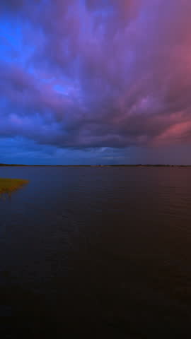 Colorful sunset sky over a lake in Florida, showing a dramatic split of blue and orange clouds reflecting in the water. Vertical Video 4k.