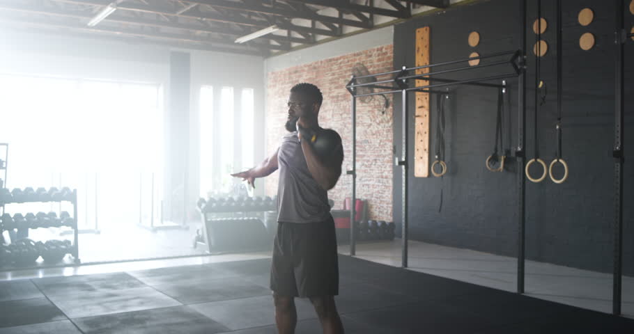 African American man swinging and pressing yellow kettlebell overhead at gym building strength. Strength, functional training, workout, fitness, resistance, power, endurance