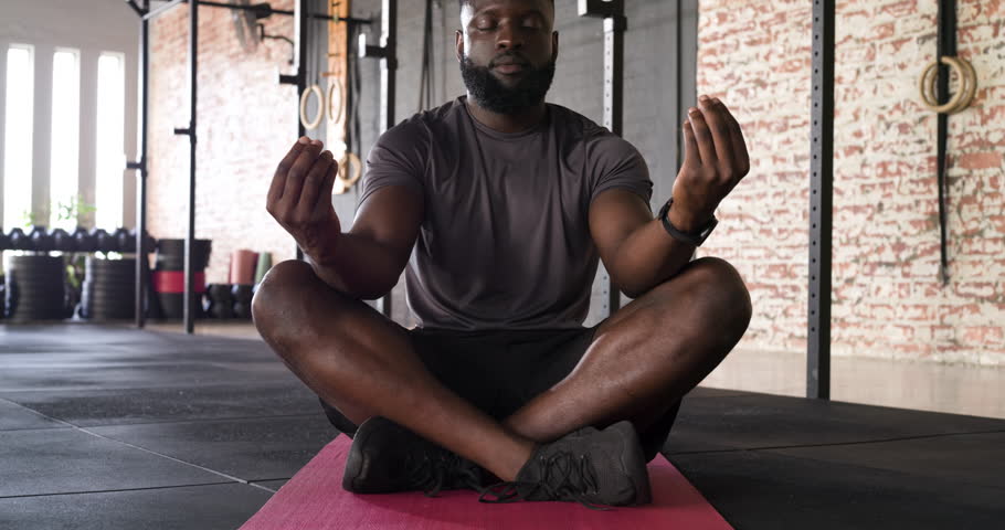 Mudra initiating African American man practicing deep breathing on pink yoga mat at gym for focus. Meditation, mindfulness, wellness, fitness, concentration, relaxation, contemporary