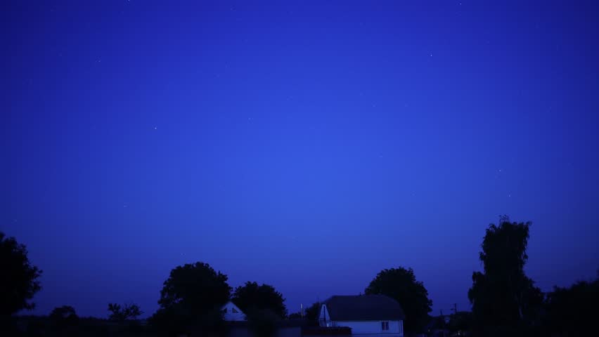 Moon rising over countryside houses and trees at twilight