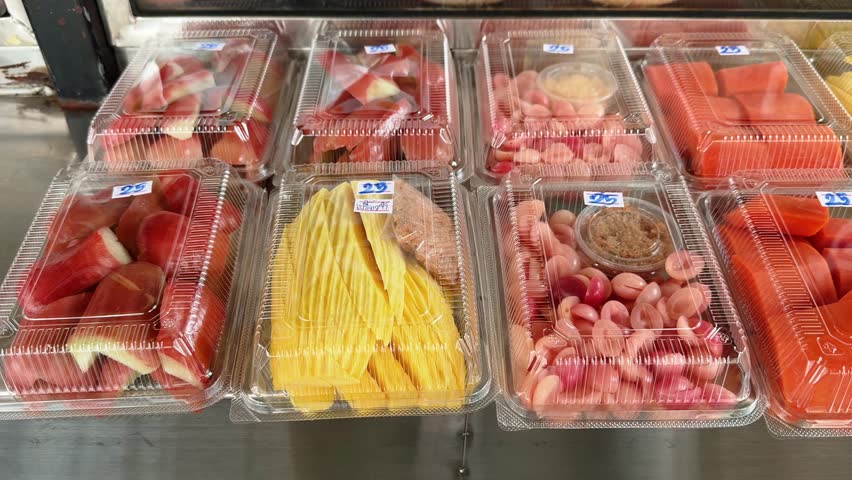 Slider motion close up of Pre-cut tropical fruits in plastic containers for sale at local street food market stand