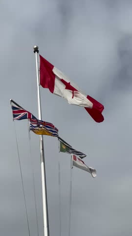 Flags flutter atop a flagpole, symbolizing national pride and regional identity, representing Canada and the unique cultural heritage of British Columbia against a cloudy backdrop, tc01