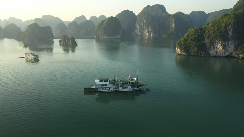 Traditional cruise boats navigating limestone karst seascape of Ha Long Bay, showcasing peaceful Vietnamese maritime culture under soft morning sunlight