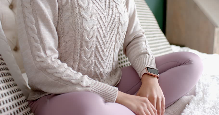 Woman straightening back and inhaling then exhaling on bed wearing knit sweater for relaxation. Meditation, mindfulness, relaxation, wellness, calmness, serenity, home environment