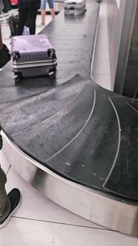 Loading luggage moving on baggage conveyor belt during post flight unloading. Travel bags advance toward claim area, passengers wait for returning items. 