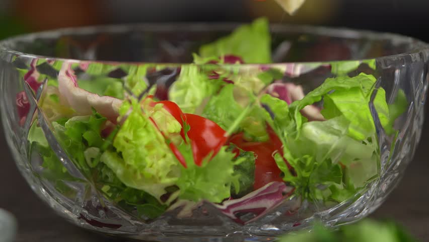 Hand squeezes lemon juice into vegetable salad with mixed lettuce leaves and tomatoes. Cooking food. Vegetarian dish