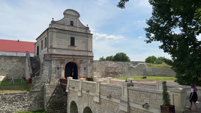 Ternopil, Ukraine - August 7th, 2025: A magnificent stone fortress gatehouse, featuring a distinctive Baroque gable, stands with a stone bridge leading to it, under a bright sky with scattered clouds