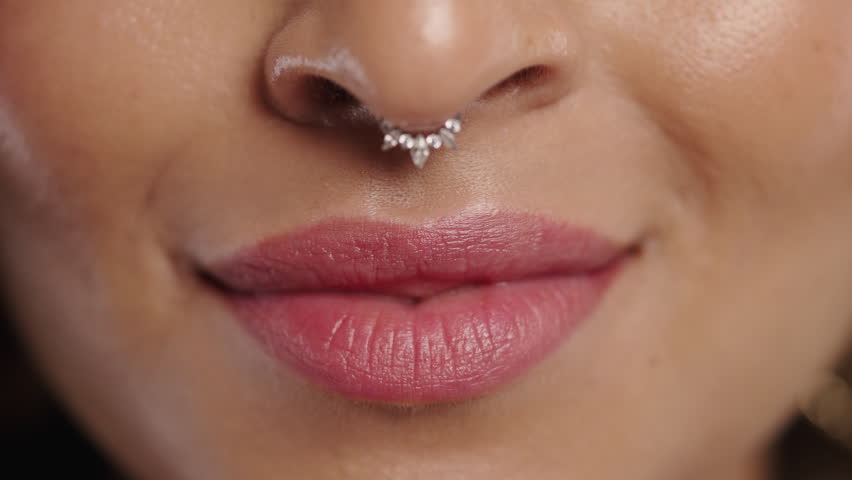 Close-up of smiling biracial woman with septum piercing and natural lips. Beauty, self-love, authenticity, modern femininity.