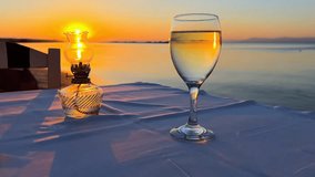 A tranquil scene with a wine glass and oil lamp on a table by the water, reflecting the vibrant colors of a sunset. Perfect for romance, dining, or travel themes. - Powered by Shutterstock - Get 15% off with code: PIKWIZARD15