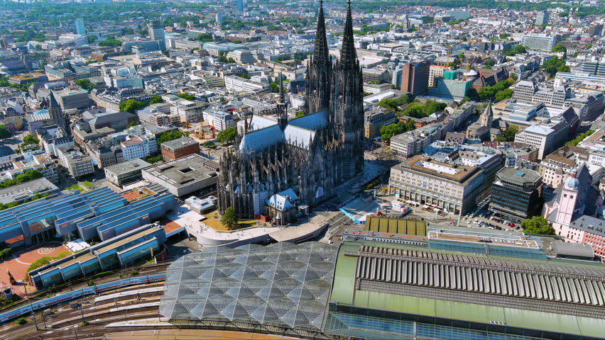4K drone view of Cologne Cathedral and Hauptbahnhof - twin spires dominating the city center. Gothic UNESCO icon framed by rail tracks and modern roofs over bustling Cologne Germany.