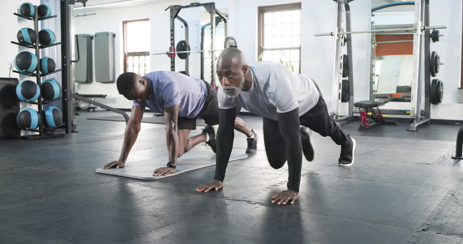 African American male trainer and trainee warming up performing mountain climbers at gym coaching. Strength, mentorship, fitness, exercise, motivation, wellness, athleticism