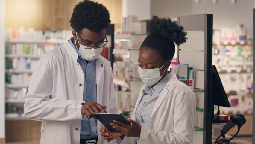 African American man woman pharmacy consultants coworking professional health care workers doctors drugstore indoors medicine inventory male female physicians in medical mask covid looking at camera
