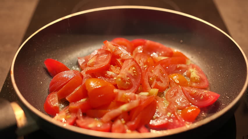 Tomatoes for an omelet are fried in a non-stick frying pan, a cook stirs tomatoes with a wooden spatula, footage for stories about home cooking and culinary inspiration
