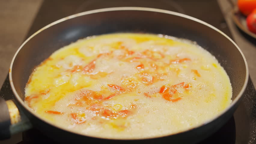 Close-up of a frying pan with scrambled eggs and tomatoes with herbs, breakfast visualization footage of cooking breakfast at home, real-time video