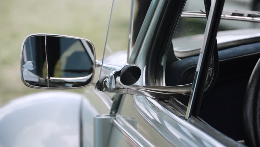 Side view mirror near manual side window of retro car closeup. Manual chrome exterior elements of old vintage car in parking lot on sunny day.