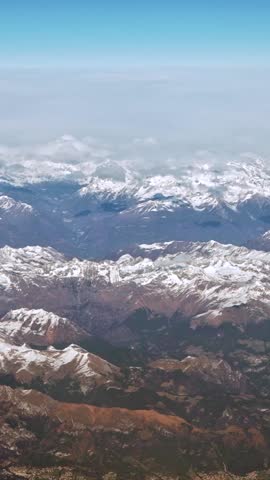 Vertical Above peaks with clouds, capped Alps with rugged mountain peaks extending across landscape. Higher elevations are covered in a light dusting of snow, giving the mountains a frosted appearance