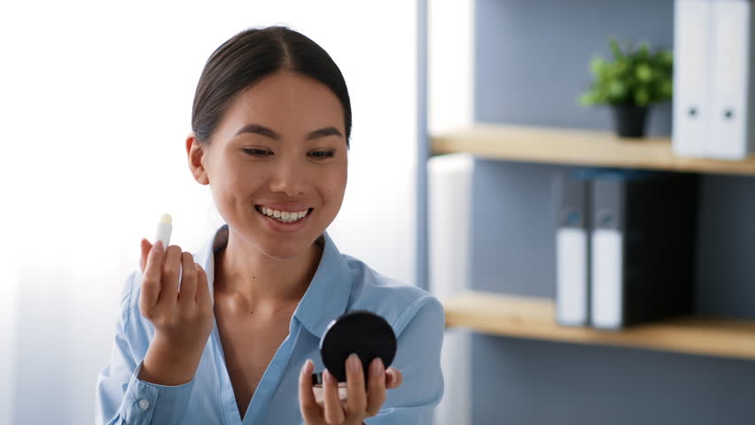 Young Asian woman applying lipstick while preparing for work in the office