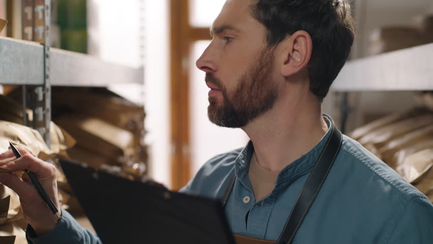 Close up focused Caucasian businessman coffee factory worker small business owner man male holding clipboard write pen check inventory aroma supplies controls storage beans production stock checklist