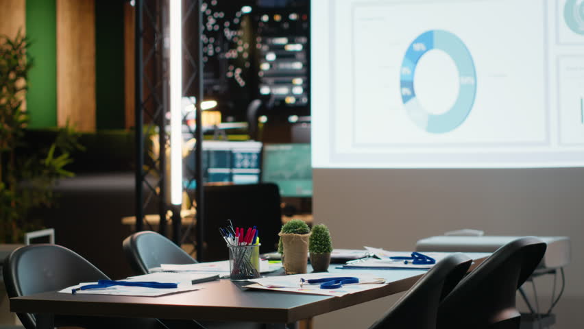 Empty boardroom space of the enterprise with forecasting reports and digital graphs running on a huge projection board late at night. Establishing management goals and targets.