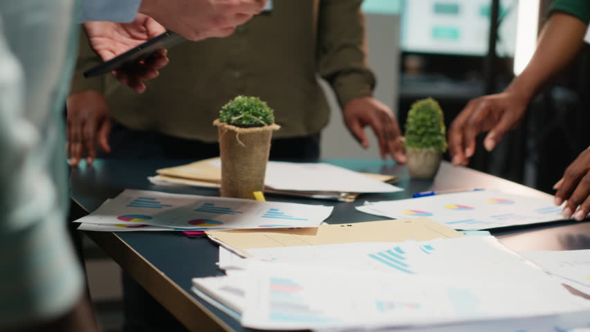 Business consultants team meeting after hours to review diagrams and assess risks, exchanging feedback and collaborating on insights backed by business intel. Forecasting predictions. Camera B.