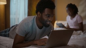 African American family husband using laptop wife digital tablet evening bedroom ethnic couple relaxing lying bed weekend gadget addiction scrolling social media watching device separation home night - Powered by Shutterstock - Get 15% off with code: PIKWIZARD15