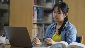 A young, tired Asian female student rubs her eyes due to strain while studying late on her laptop in a library, conveying concepts of stress, fatigue, overwork, and eye strain. - Powered by Shutterstock - Get 15% off with code: PIKWIZARD15