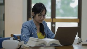 A young, tired Asian female student rubs her eyes due to strain while studying late on her laptop in a library, conveying concepts of stress, fatigue, overwork, and eye strain. - Powered by Shutterstock - Get 15% off with code: PIKWIZARD15