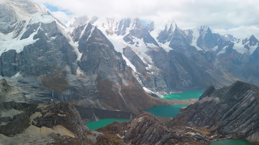 A breathtaking aerial reveal shot soars over the Andes to show the three famous turquoise glacial lakes Tres Lagunas of the remote and beautiful Huayhuash trek in Peru.