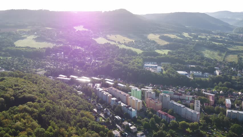 Drone pans right revealing apartment blocks nestled among trees and hills on a sunny morning in Decin, Czech Republic.